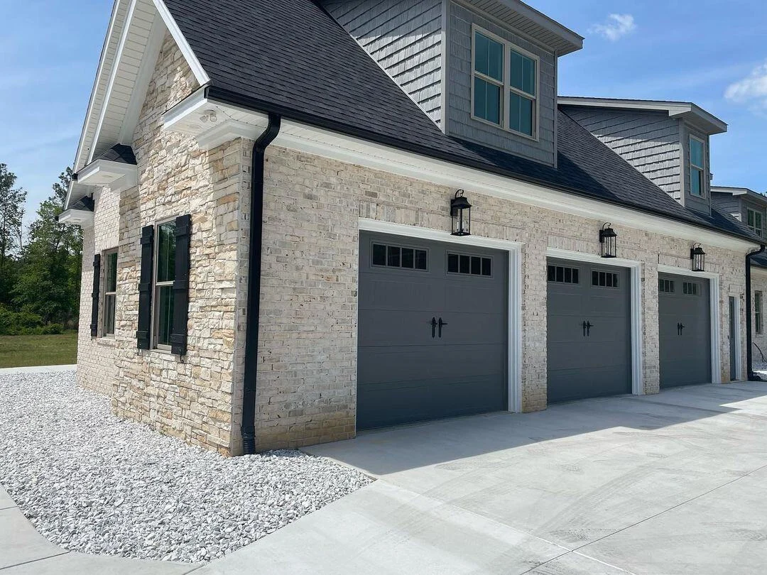 Three graphite carriage-style garage doors with windows on a stone home, new garage door installation Ottawa