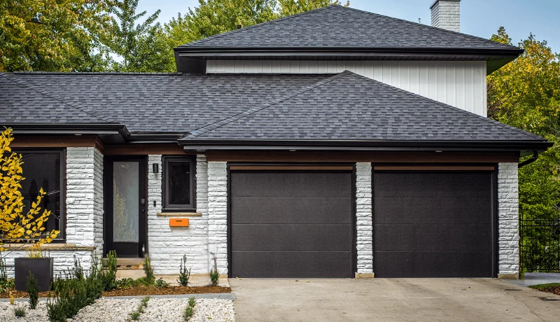 Two black flush modern garage doors on a white stone bungalow, modern garage door replacement Ottawa