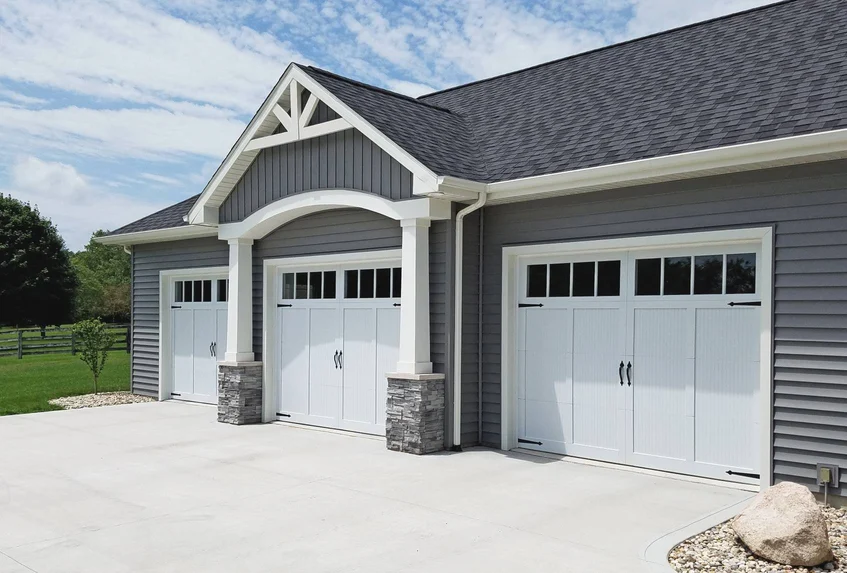 White overlay carriage house garage doors with black hardware on a grey home, carriage-style garage door installation Ottawa